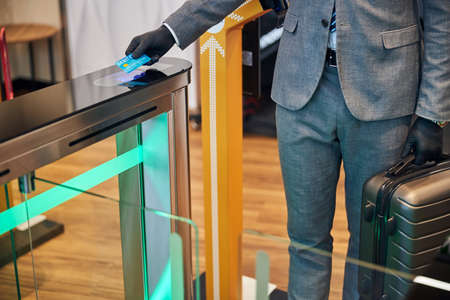 Cropped photo of a traveler with baggage scanning his debit card while going through an electric...