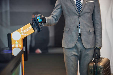 Businessperson with a suitcase paying money for the entry with a credit card at a pay gate of an airportの写真素材