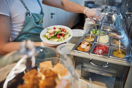 Waiter in white protective gloves extending his arm to the dishes on the display while holding a...