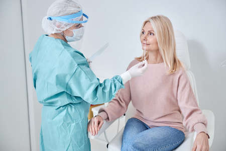 Qualified medical lab technician collecting mucus from the female patient nose for a PCR testの素材 [FY310159315263]