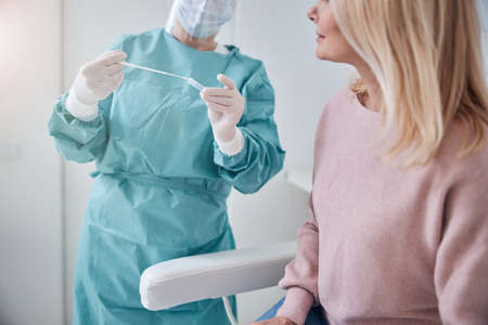 Cropped photo of a lab technician placing the throat swab in a sterile container in front of the patientの写真素材