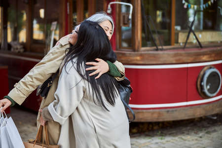 Charming woman embracing best friend and smiling while holding shopping begsの写真素材