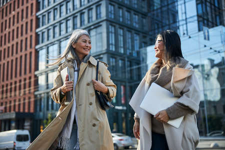 Two beautiful stylish women holding notebooks and smiling while spending time outdoorsの写真素材