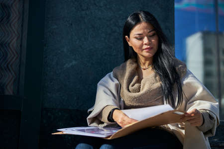 Charming brunette lady holding folder with papers while working on project outdoorsの写真素材