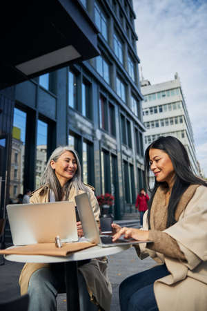 Charming female friends sitting at the table with modern notebooks and smilingの写真素材