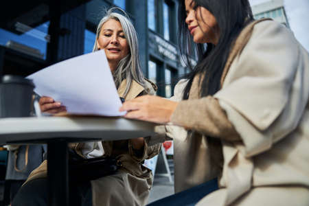 Charming female business colleagues sitting at the table with coffee and analyzing financial reportの写真素材