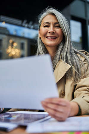Beautiful businesswoman looking at camera and smiling while holding sheet of paperの写真素材