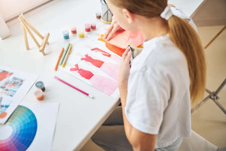 Back view of a blonde girl matching the samples of fabrics to her dress sketches