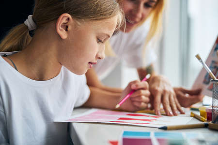 Side view of a girl with a pencil in her hand and her mother scrutinizing sketches