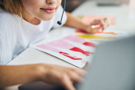 Cropped photo of a blonde Caucasian girl with a tiny mike sitting at the deskの写真素材