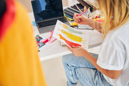 Cropped photo of a female fashion designer with dress sketches sitting cross-legged at the desk