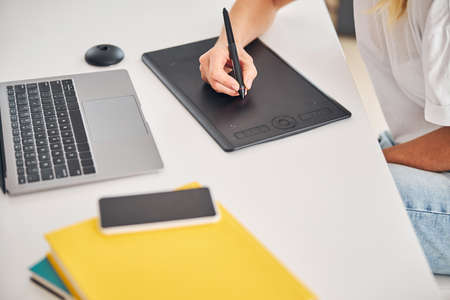 Cropped photo of a woman holding a stylus in one hand over the graphics tablet