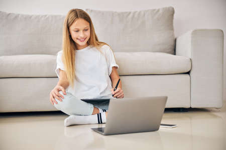 Front view of a lovely smiling female artist with a digitizer and a stylus sitting before the laptop