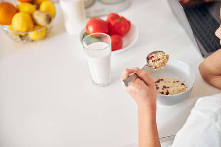 Cropped photo of a girl in a t-shirt holding a spoon of porridge in her hand
