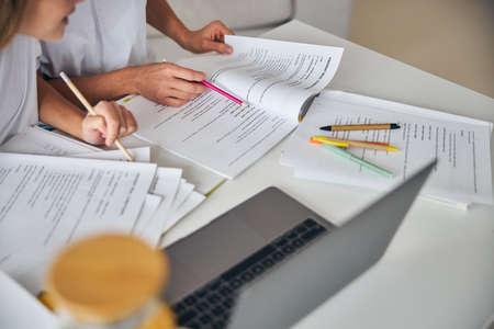 Cropped photo of a woman pointing out a sentence in a book to a teenage girl with a pink pencil