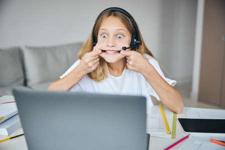 Student pulling the sides of her mouth with the fingers while making a goofy expression in front of...