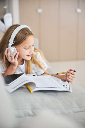 Learner of English taking pleasure in listening to the melodies through headphones while pointing an eco-pen to the workbookの写真素材