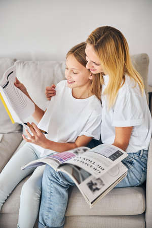 Adult embracing an underage student while sitting in the corner of a sofa and reading a textの写真素材