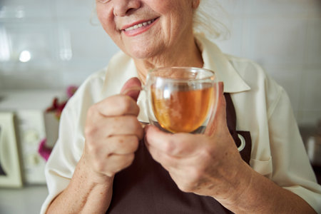 Close up of smiling elderly lady with cup of hot drink in her hands expressing positive emotionsの写真素材