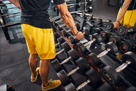 Cropped photo of a professional male athlete standing in front of the dumbbell storage standの写真素材