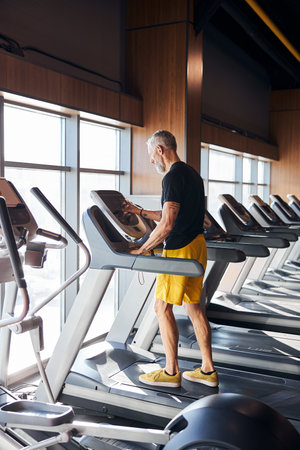 Gray-haired bearded Caucasian professional male athlete starting his cardio workout in a modern...