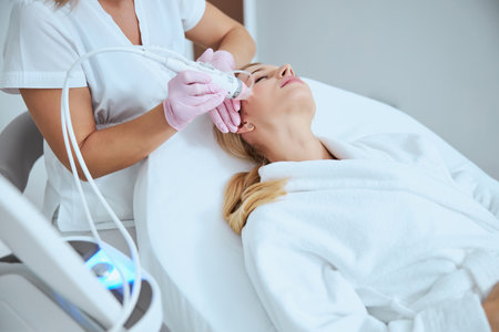 Professional Caucasian dermatologist conducting a microneedling procedure on her young patient using a modern beauty deviceの写真素材