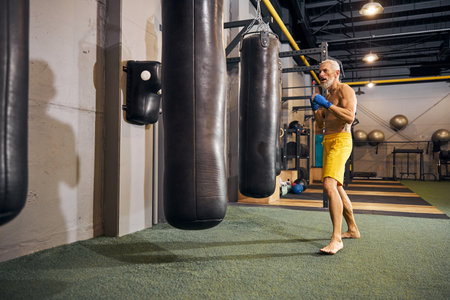 Full-sized portrait of a focused barefoot kickboxer standing before the punching bags in an upright stanceの写真素材