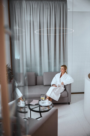 High-spirited young woman with a smartphone sitting cross-legged in the foyer of a modern wellness centerの写真素材