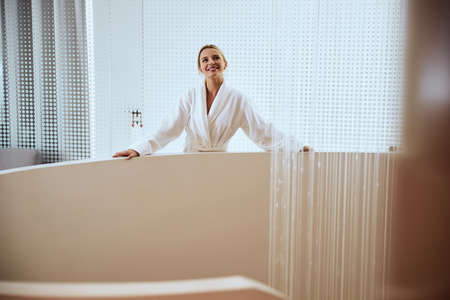 Waist-up portrait of a smiling young spa client leaning on the handrail of the staircase