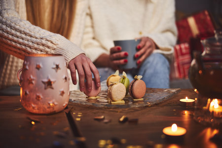 Cropped head close-up of girl enjoying hot drink and macaroons together with mother at homeの写真素材