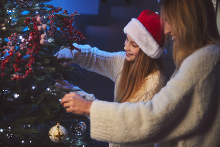 Cheerful cute teenage girl is decorating flat for New Year together with her beloved motherの写真素材