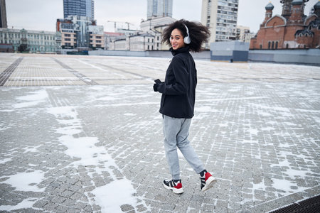 Cheerful sportswoman beginning her running with a smartphone and headphones on a square covered with...