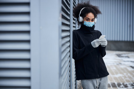 Person in hospital mask taking a look away from a mobile phone while clicking on itの写真素材