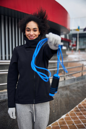 Person holding out a blue skip rope with left hand and offering it to someone outside the frame