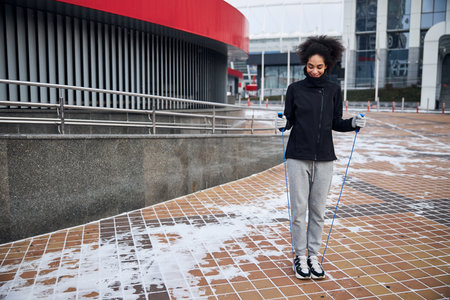 Woman standing on a skipping rope while dragging its handles up with a joyful smile