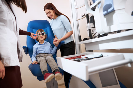Caring parent folding her palms around kid hand while he sitting during the lens fitting processの写真素材