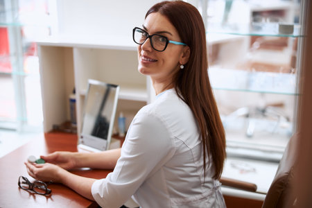 Female eye specialist with a long brown hair turning with a smile while having contacts in her handsの写真素材
