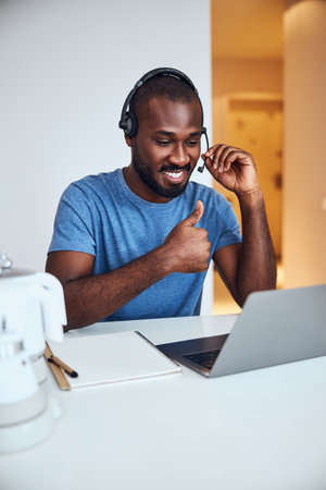 Glad conference participant adjusting his microphone while showing thumbs-up to a laptop camera