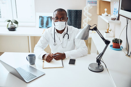 Man working in a hospital and sitting behind his table with hands on a notebookの写真素材