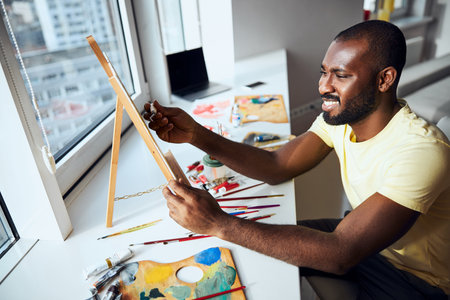 Creator using a painting knife for making a picture of a small easel standing on a windowsillの写真素材