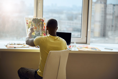 Afro-American male sitting with a turned back to camera and making corrections to his work