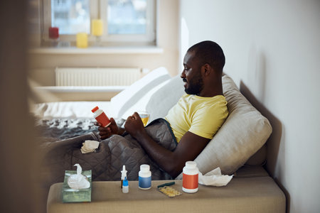 Person feeling sick and recovering in bed with a teacup and container of medicine in handの写真素材