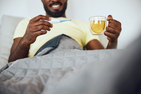Man checking the temperature measurements on an electronic thermometer while having a tea drink