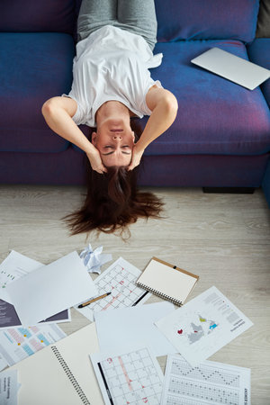 Top view of tired young female lying on sofa upwards after hard working day with documents at home during isolationの写真素材