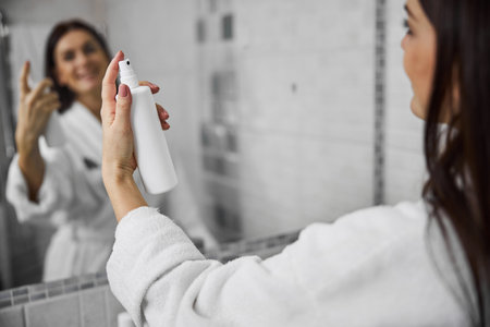 Cropped head close up of female hand holding bottle with treatment and applying it on hair in bathroomの写真素材