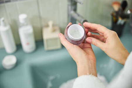 Cropped head close up top view of female hands holding jar with treatment for skin at home