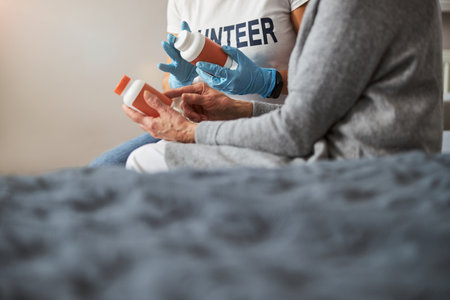 Orange containers with tablets in the hands of a pair of adults sitting on a bedの写真素材