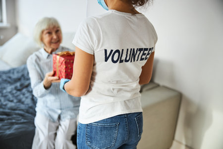 View from the back of a social worker in a white shirt pleasing a senior lady with an unexpected giftの写真素材