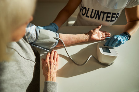 Cropped photo of a female volunteer measuring the pensioner blood tension with an automatic manometerの写真素材