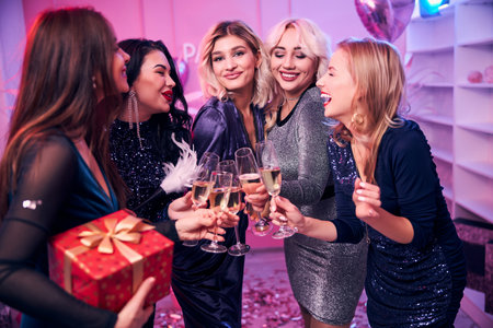 Five pleased attractive dressy female coworkers raising glasses to their success at the office partyの写真素材